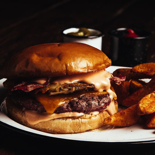 Hamburguesa de la casa con tocino y queso cheddar derretido, con papas gajo