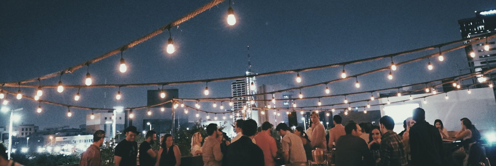 Noche de evento en la terraza, llena de gente bajo las series de luces